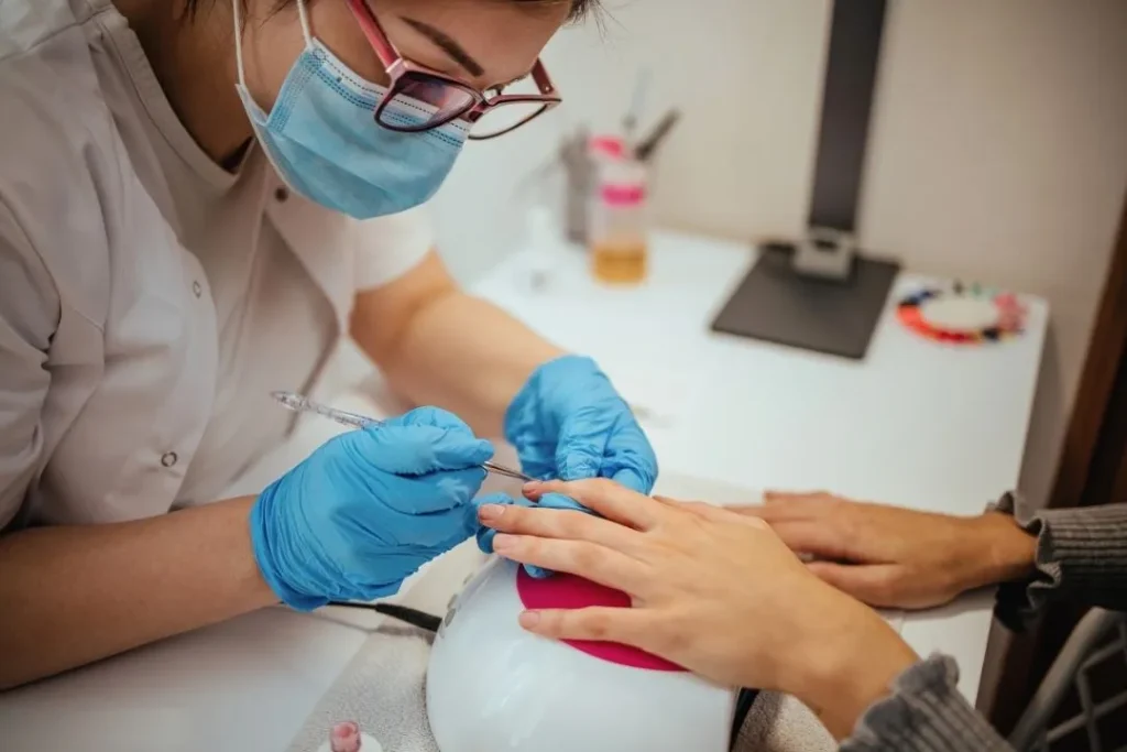 Stylistka wykonująca manicure hybrydowy klientce w profesjonalnym salonie paznokci