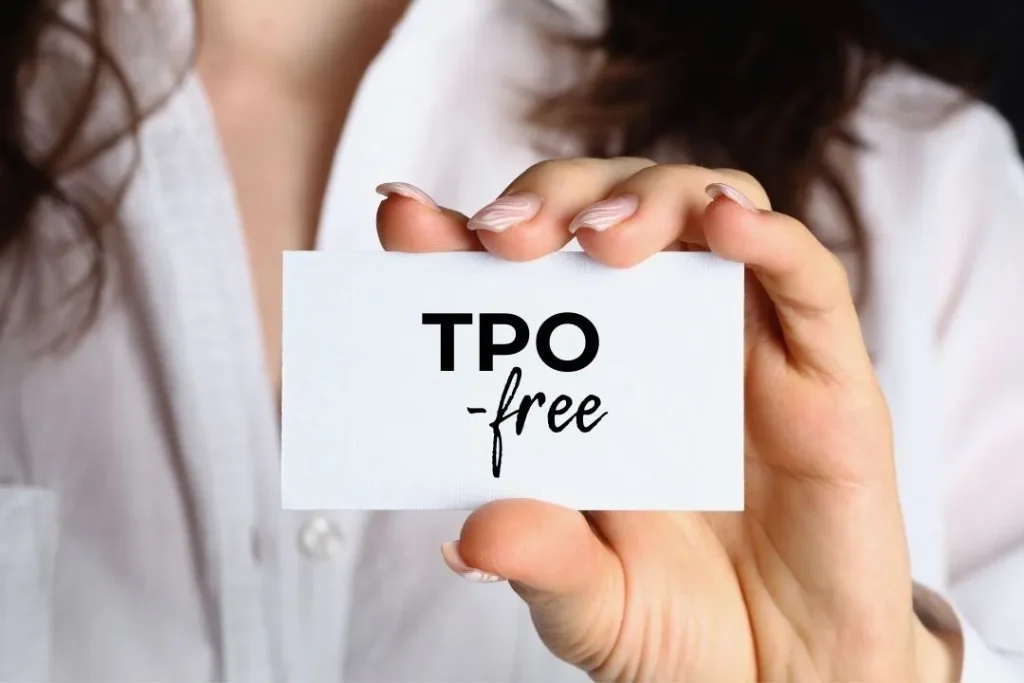 Zbliżenie na dłoń trzymającą kartę z napisem TPO-free, symbol bezpiecznych lakierów hybrydowych wolnych od zakazanej substancji